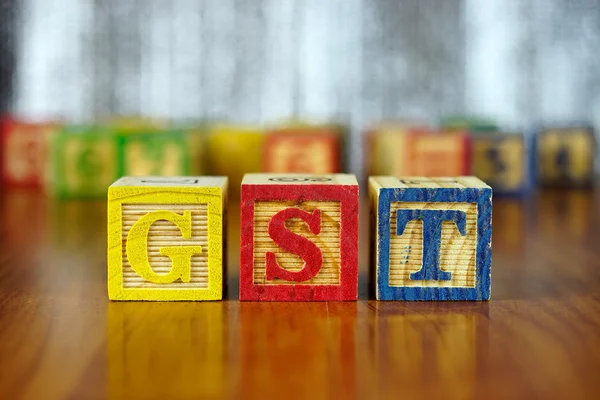 Palavra de GST soletrado com blocos alfabeto de madeira coloridos.Foco seletivo, profundidade rasa de campo . — Fotografia de Stock