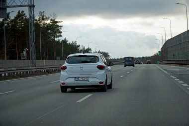 Varşova, Polonya - 2 Şubat 2025 - S17 karayolunda bulutlu bir gökyüzünün altında giden beyaz araba