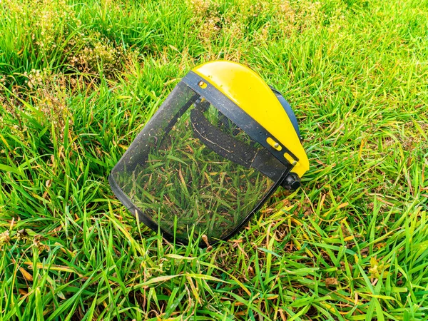 芝刈り機で作業するための保護面マスク 保護マスクだ 緑の芝生を切断するためのトリマー 横に芝生を刈る 庭師の道具だ 工作機械だ 庭で働くために — ストック写真