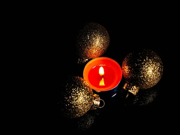 Christmas candle flame with golden toys in the dark. The flame of a wax candle. Golden decorative balls. Merry Christmas. New Year\'s Holidays. Winter vacation. Black background. Night darkness.