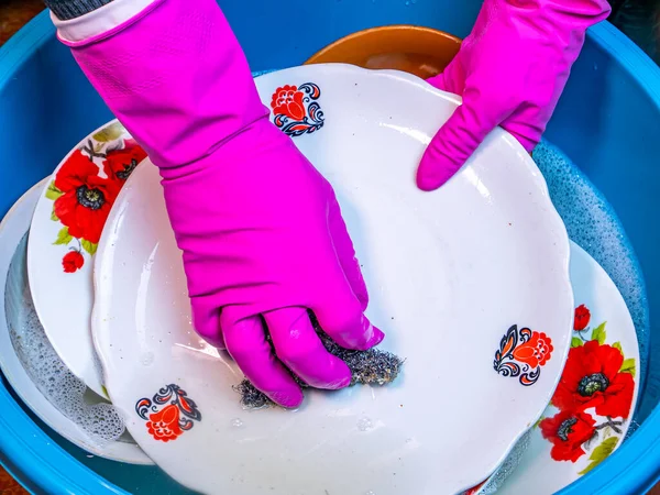Plastik bir kasede el yıkama aletleri. Bulaşık deterjanı. Bulaşıkçı. Plastik bir kasede el yıkama tabağı. Ev hanımı. Hizmetçi. Kadın ev işi mutfak işi. Ev eldivenleri..