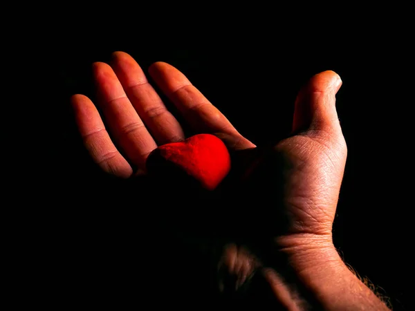 黒の背景に手でバレンタインデーのハートシンボル 赤いハートのシンボル バレンタインデー 男性の手の手のひら 愛の感情 黒の背景 男と女の関係 — ストック写真