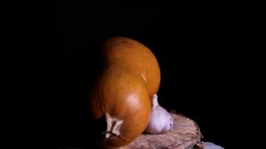 Balkabağı turuncu ve sarımsak başı karanlıkta dönüyor. Balkabağı sebzesi. Bir baş sarımsak. Baharatlı yemek. Vejetaryen yemeği. Tarım hasadı. Ev mutfağı. Cadılar Bayramı. Video.