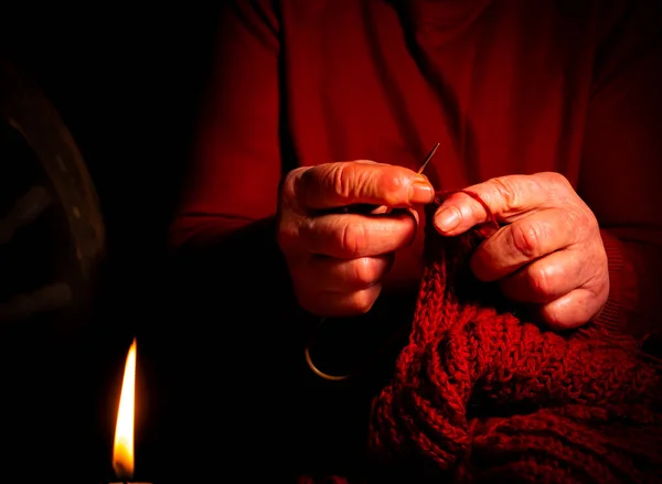 Hand knitting with woolen thread by candlelight. Knitting needles. Woolen thread. Old man\'s hands. Handwork. Weave warm clothes. Manual creativity. Self made. The flame of a wax candle.