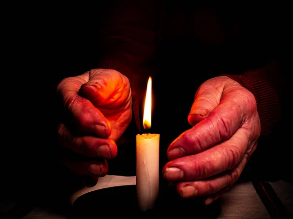 The flame of a burning wax candle in the hands of an old man. The flame of a wax candle. Fire in the dark. Day of Remembrance. A minute of silence. Funeral services. Sorrows on Memorial Day.