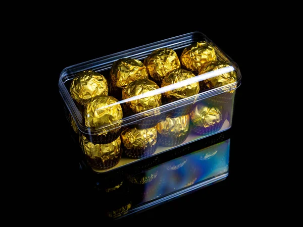 Una caja de chocolates redondos en una envoltura dorada sobre un fondo negro. — Foto de Stock