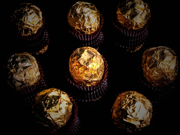 Caramelle di cioccolato rotonde in un involucro d'oro su uno sfondo nero. — Foto Stock