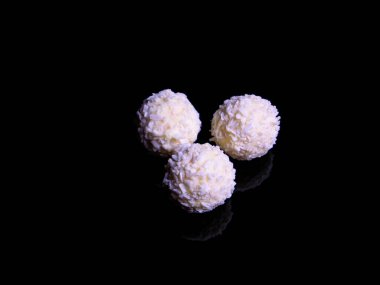 Siyah arka planda hindistan cevizi taneleri olan yuvarlak beyaz şeker. Çikolatalı şeker. Beyaz çikolata. Hindistan cevizi gevreği. Yuvarlak beyaz dondurma. Dondurmalı dondurma. Tatil hediyesi. Siyah üzerine beyaz.