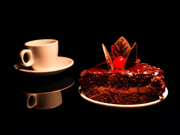 Chocolate cake with cherries and a cup of coffee on a black background. Coffee in a cup. Coffee cup and saucer. Chocolate cake. Lived with cherries. Cake dessert. Sweet creamy dessert.