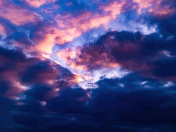 Pink clouds in the rays of the sunset. Sunny sunset. Evening twilight. Blue sky. Atmospheric phenomenon. Cumulus clouds. Sunlight. Weather. Background image. Natural beauty.