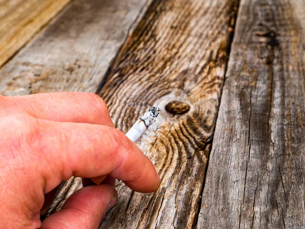 Cigarette butt in a smokers hand on a wooden background.