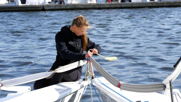 A young athlete, a blonde girl in a tracksuit, is mooring a yacht on the river on a cool, windy day. — Stock Photo, Image