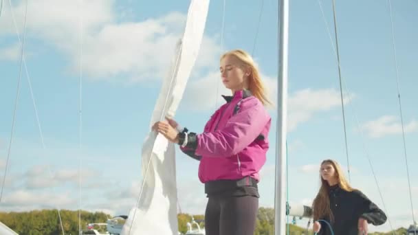 L'équipe féminine de voiliers sur le quai met conjointement la grand-voile sur le mât d'un yacht de sport blanc pour la régate de la mer du Nord. — Video