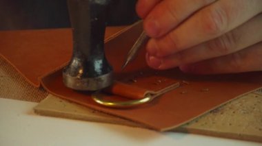 Terzilerin elleri çekiçle ve çekiçle, yavaş çekiçle çantanın sapında iplik için delikler açıyor.