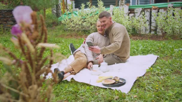 Slavische man en vrouw op een picknick op de binnenplaats van een huis in het dorp neem een selfie op een smartphone. — Stockvideo
