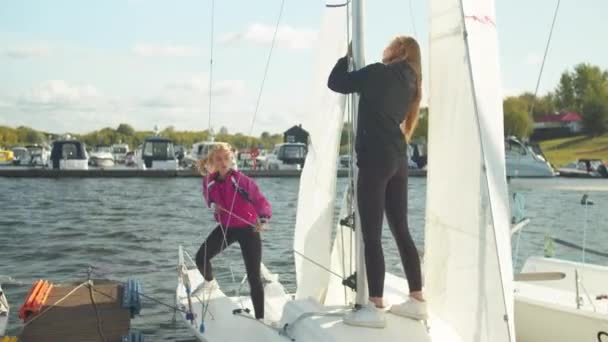 Командная работа юных спортсменов. Девушки вместе поднимают парус на собственной быстрой спортивной яхте. — стоковое видео