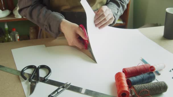 Um alfaiate em um avental corta padrões com tesoura para criar roupas exclusivas para o negócio da família. — Vídeo de Stock