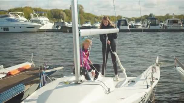 Ve větrném počasí v přístavu, ženy plachtění tým připravuje jachtu k účasti na řece regata. — Stock video