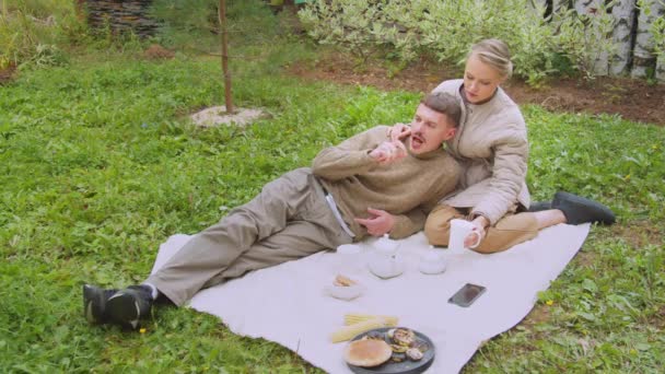 Een man en vrouw hadden een picknick in de familie tuin in de buurt van hun eigen dorpshuis. Ze drinken thee, eten snacks.. — Stockvideo