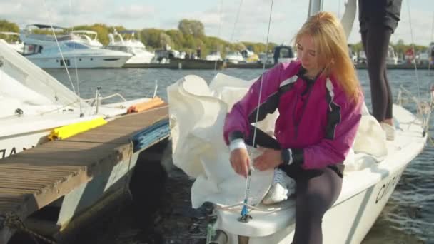 Женщины-спортсменки проверяют паруса и другое оборудование на своей белой спортивной яхте перед тем, как покинуть пристань для регаты — стоковое видео