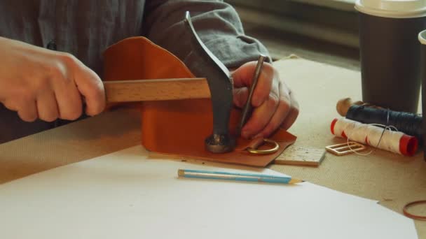 Con un núcleo y un martillo, el curtidor perfora agujeros para coser una bolsa exclusiva de cuero genuino. Movimiento lento. — Vídeos de Stock