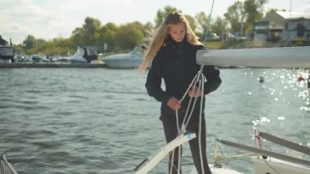 Langhaarige schöne Mädchen spannt ein Seil durch einen Baum, bereitet sich auf einen Segelwettbewerb auf einer weißen Jacht vor — Stockvideo