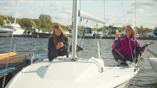 Giovani ragazze con smartphone siedono a bordo di un costoso yacht sportivo e scattano selfie per il loro video blog. Rallentatore. — Video Stock