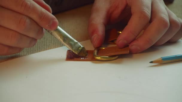Detailní záběr rukou koželužů pracně lepících dohromady zapínání dámské kožené tašky s koženým lepidlem a štětcem. — Stock video