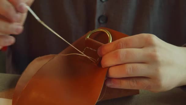 A professional tailor tanner sews an accessory attachment to a bag made of genuine leather. Close-up, slow motion. — Stock Video