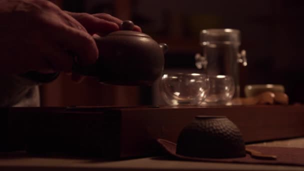 Närbild av handen på en asiatisk mästare hälla te i koppar stående på chaban, från en riktig tekanna gjord av yixing lera. — Stockvideo