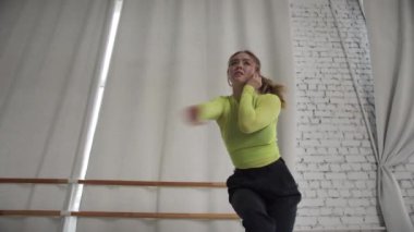 Güzel, çağdaş bir dans, bir kız dansçıyı çatı katında, duvarlara ve perdelere yaslanmış, aşağıdan çekim yaparken gösteriyor.