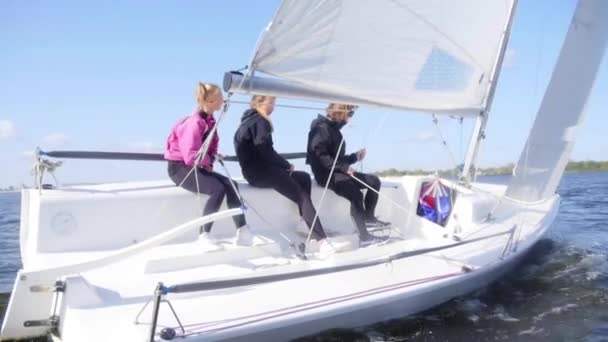 Two girls and a guy manage a small yacht during a river trip in early autumn. Dynamic shot with effect of slow motion. — Stock Video