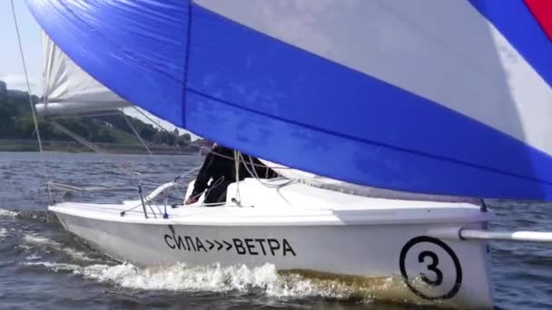 Tir au ralenti. Deux jeunes filles et un gars montent sur le lac sur un yacht, devant lequel il y a une grande voile multicolore — Video