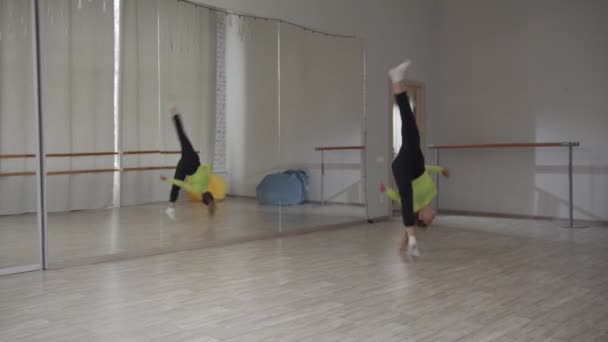Movimento lento. Menina loira bonita esportiva faz um salto acrobático em um salão de dança com um espelho . — Vídeo de Stock