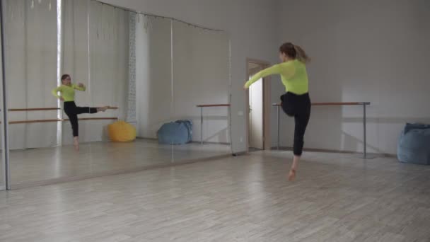 Um conjunto de belos movimentos na dança contemporânea. Uma rapariga de t-shirt amarela e calças pretas está a dançar no chão do estúdio. Saltar com divisões. — Vídeo de Stock