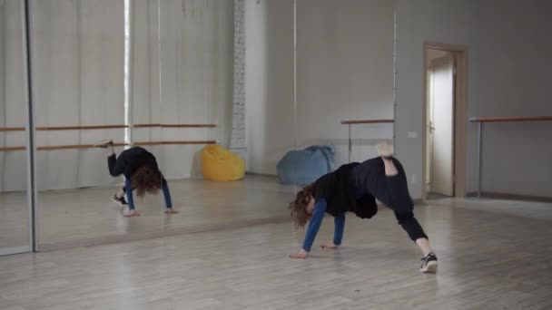 Uma garota de cabelos encaracolados na frente de um espelho ensaia sua dança para uma performance em uma competição de dança. Dança contemporânea com elementos de moda e vigília. — Vídeo de Stock