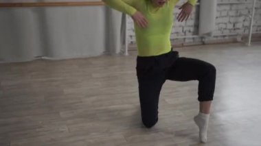 Salonda, esnek genç bir kız pencerenin yanında dans eder. Elleri ve ayaklarıyla güzel hareketler yapar.