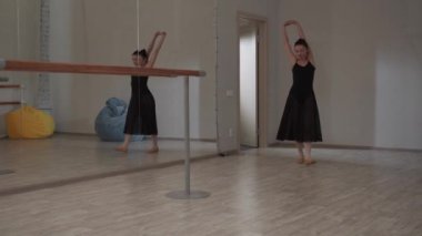 Bir balerin balo salonuna girer ve provadan önce ellerini uzatmaya başlar.