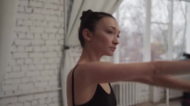 A balerina azzal kezdi a próbát, hogy kinyújtja az izmait a táncterem ablakánál, közelről. — Stock videók