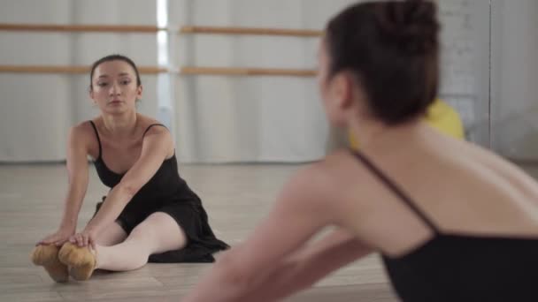 Az edzőteremben a tükör előtt a balerina kinyújtja a hátát, és ráül a spárgákra. — Stock videók