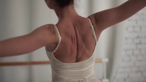 Zicht op de achterkant van een ballerina in een witte jurk dansend tegen een bakstenen muur in de hal — Stockvideo