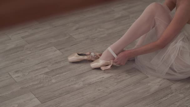 Den ballerina sidder på gulvet, sætter på pointe sko og bånd bånd bånd omkring hendes fødder – Stock-video