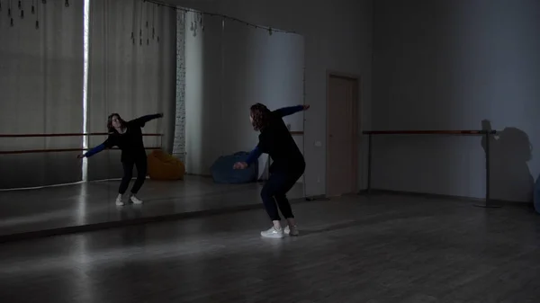 Szerokie ujęcie studia tańca, gdzie młoda dziewczyna tańczy przed lustrem w różnych kierunkach tańca współczesnego. — Zdjęcie stockowe