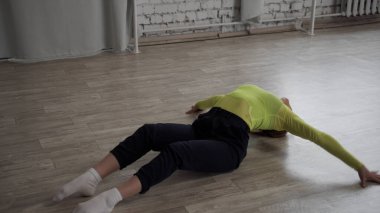 Modern dans eden sevimli dansçı kız, rahat bir dans salonunda ahşap zeminde dans ediyor.