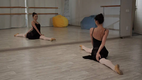 Mooi ballerina meisje toont benen strekken en splitst in de voorkant van de spiegel in de danszaal — Stockfoto