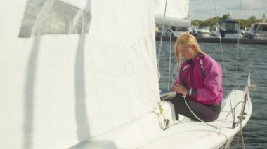 Güzel bir kız marinadan ayrılmadan önce beyaz yelkenli bir yatın iplerini çekiyor.