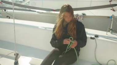 Bir spor yatında otururken güzel bir kız yelkenli teknelerinde yelkenli yarışı yapan bir nehirden önce ipi çözer.