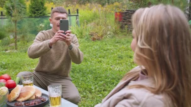 Het meisje vroeg de man om een foto van haar te nemen op haar smartphone voor haar video blog. Tijdens de lunch in het dorp. Langzame beweging — Stockvideo