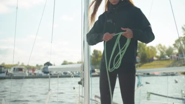 Na doca, uma jovem, muito esportista ventos cordas em torno de seu braço enquanto puxando um iate à vela para uma regata no rio — Vídeo de Stock