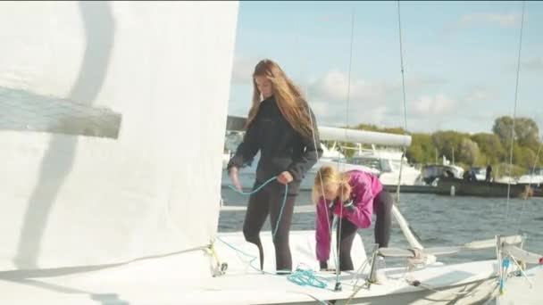 Dwie słodkie dziewczyny stoją na rufie białego jachtu sportowego i pociągnąć liny do kontroli żagiel — Wideo stockowe